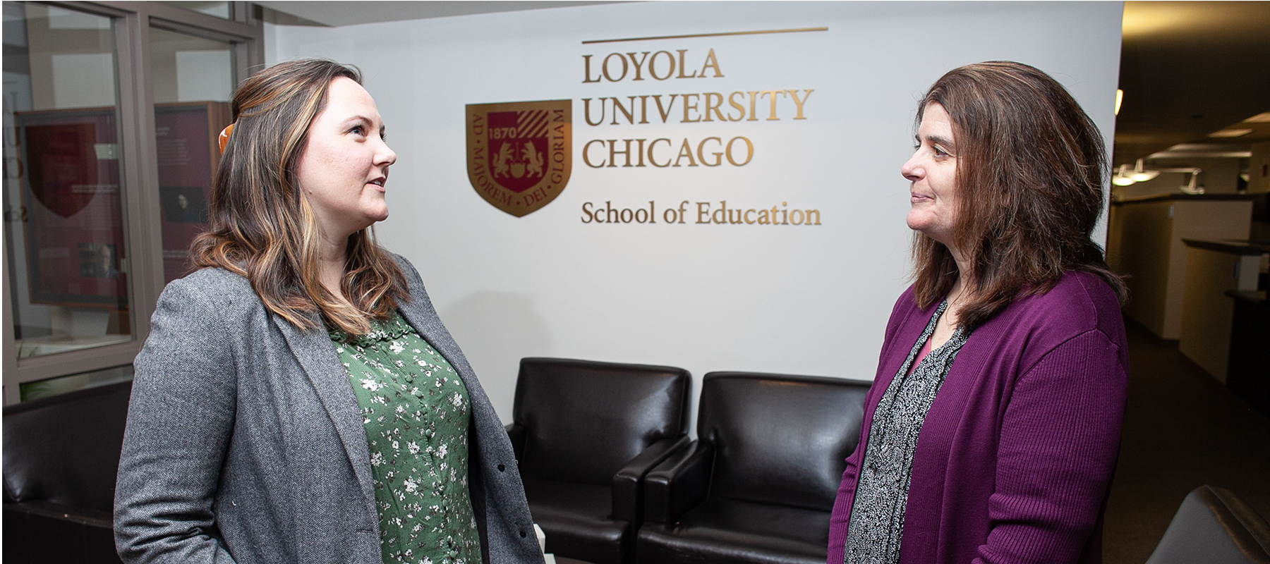 Drs Fenning and Mayworm stand in front of Loyola Chicago logo talking.